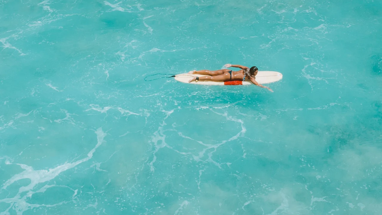 An overhead view of a surfer paddling a board through turquoise water