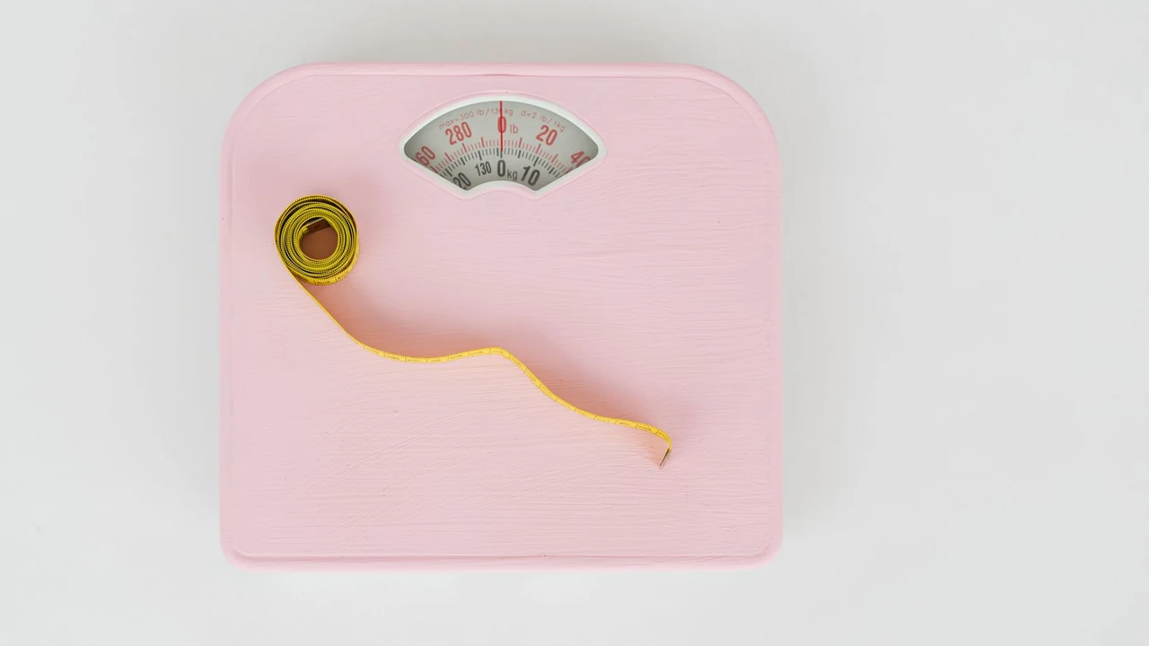 A pink bathroom scale with a measuring tape on a pale surface
