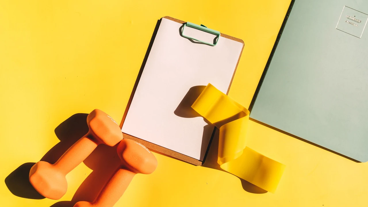 A blank clipboard beside small dumbbells and a yellow resistance band