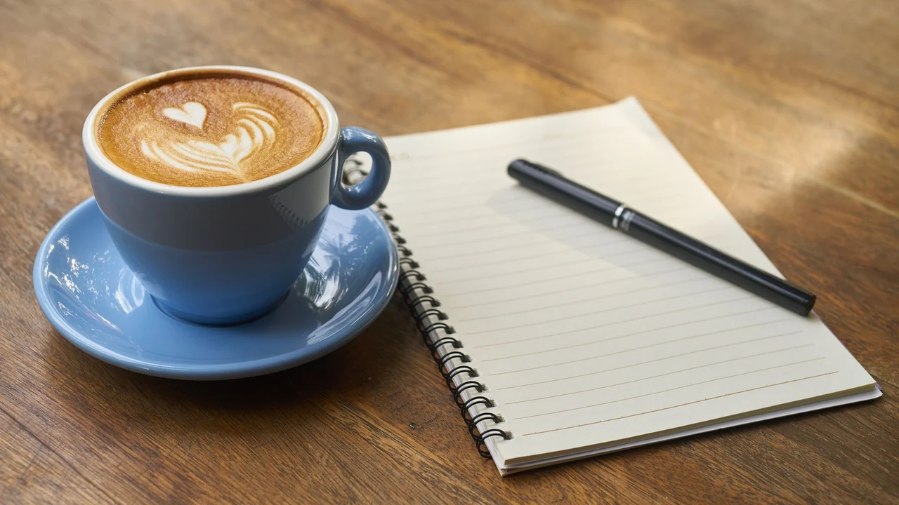 Open notebook and pen beside a cup of coffee