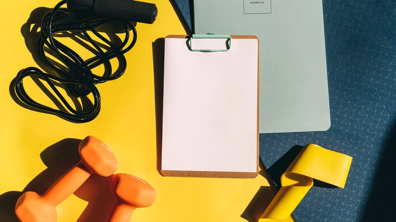 Clipboard, notebook and exercise equipment on a yellow surface