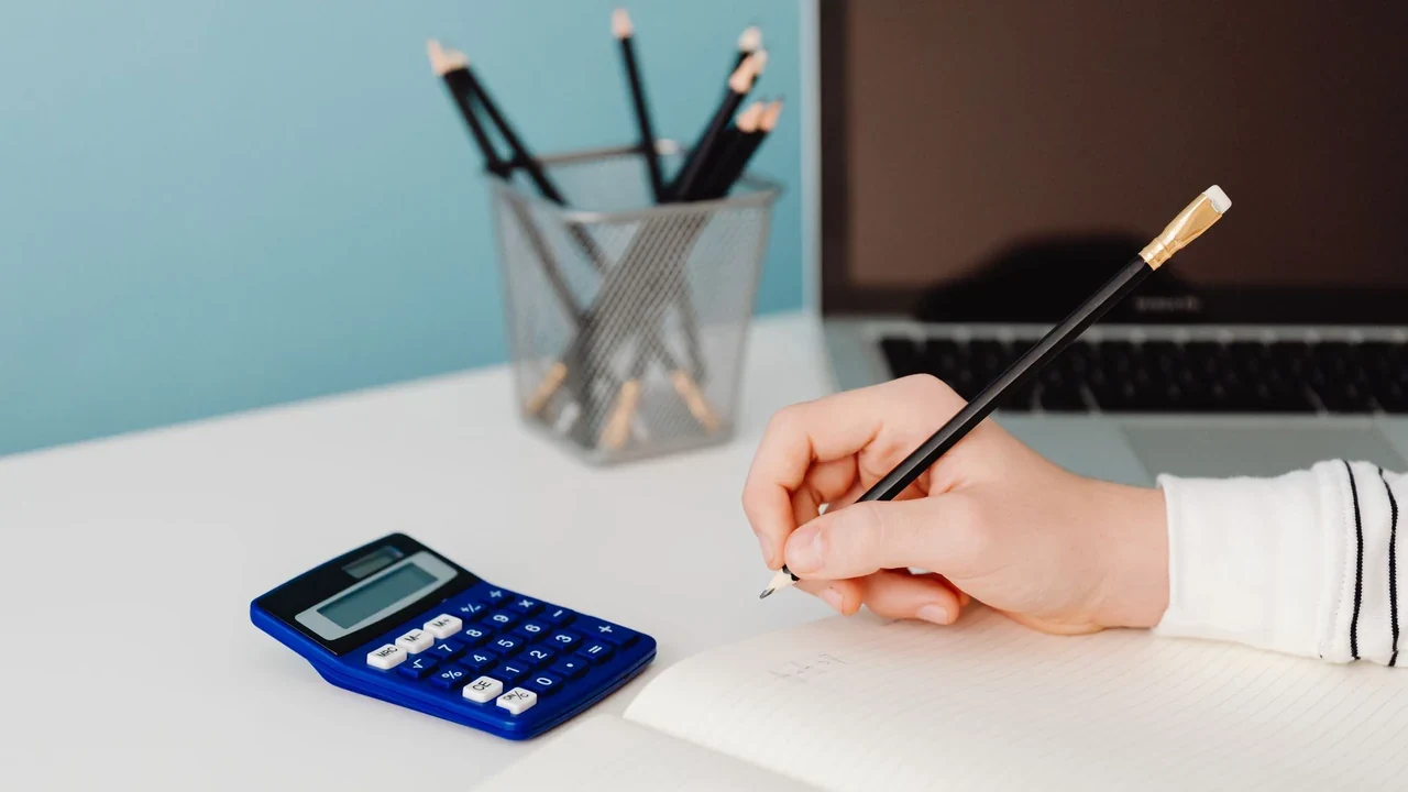 Hand writing in a notebook beside a calculator