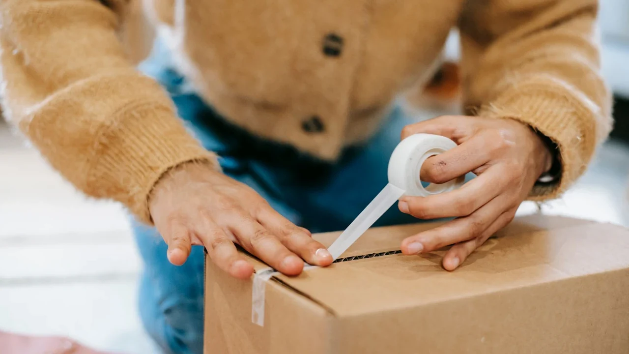 Person sealing a cardboard parcel with packing tape