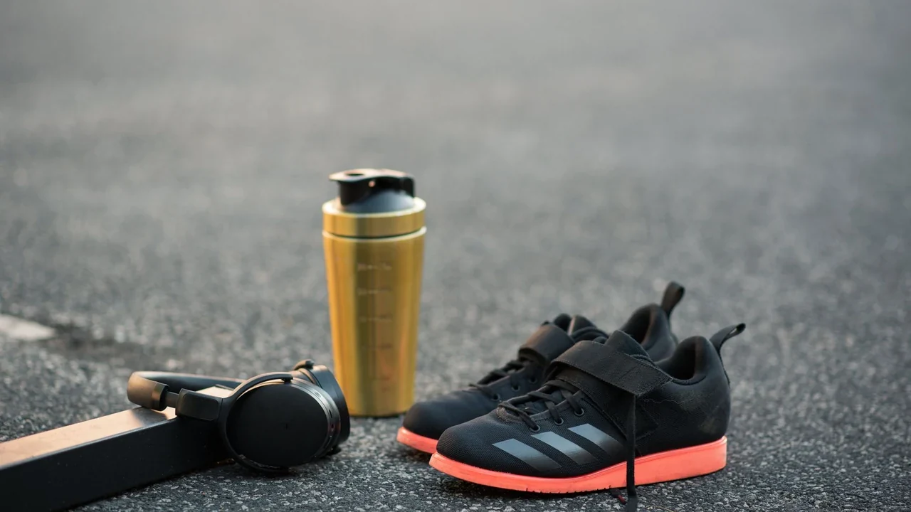 Training shoes, headphones and a yellow bottle on pavement.