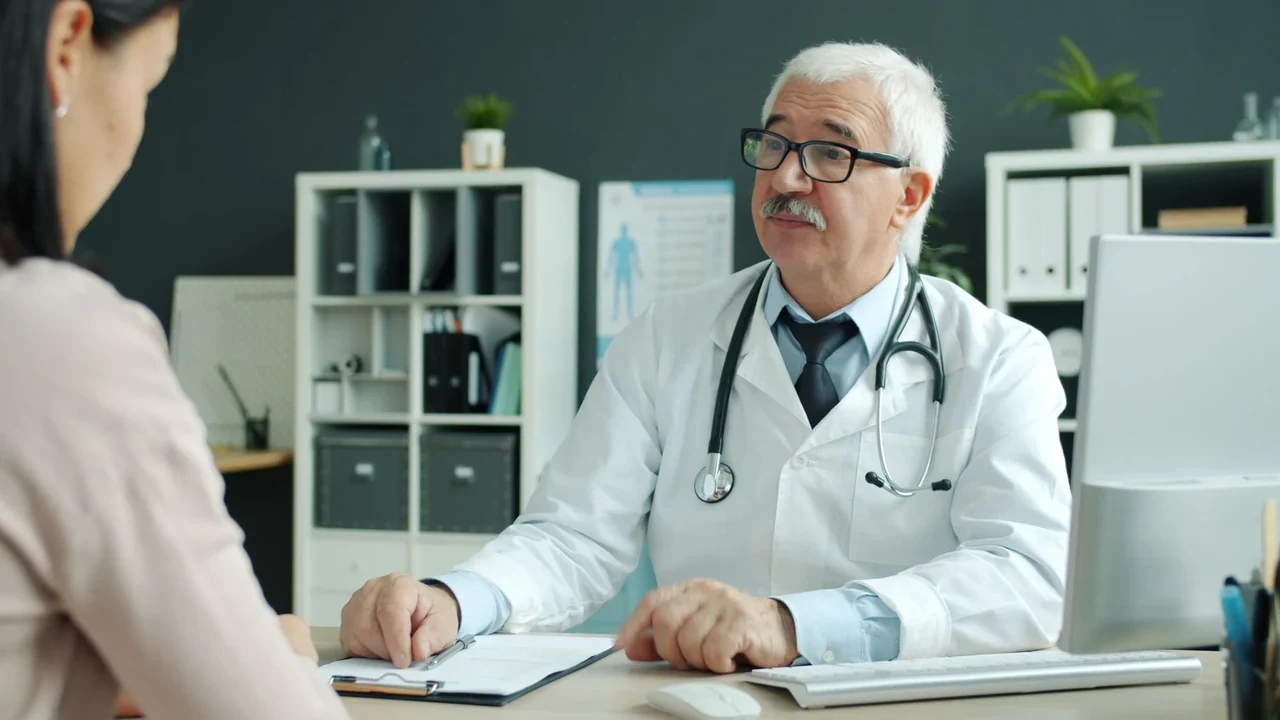A person in a white coat discussing paperwork at a consultation desk.