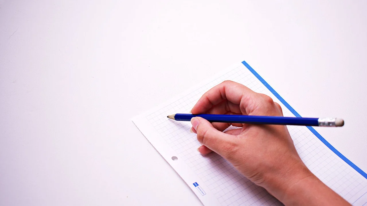 A hand writing with a blue pencil in a squared notebook