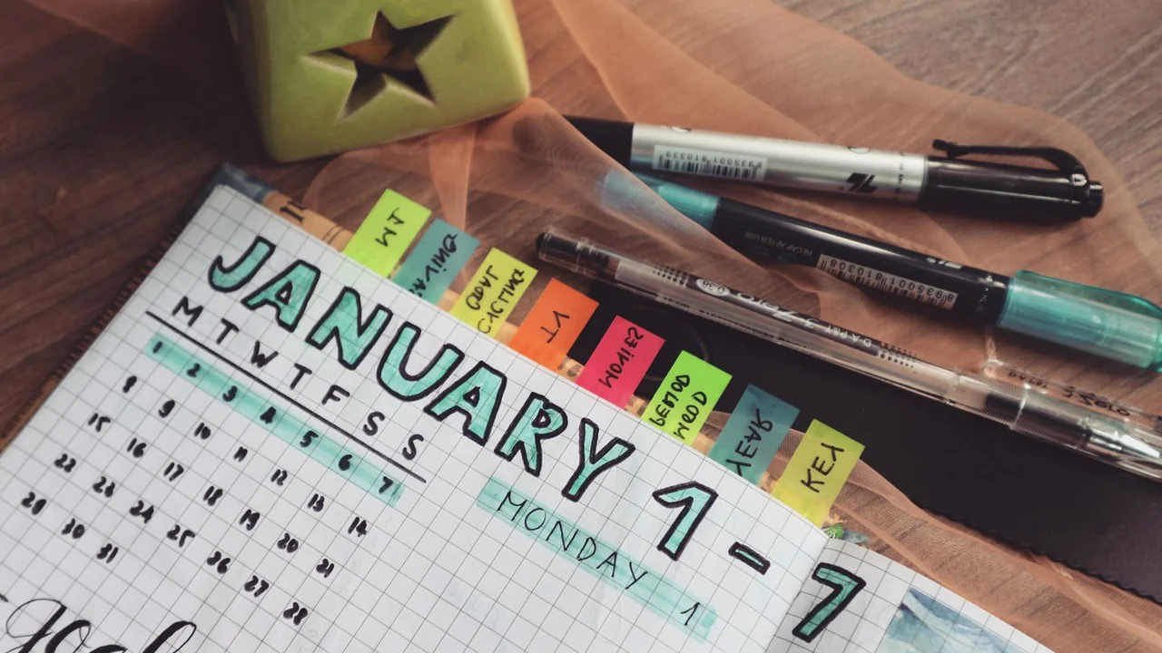 An open weekly planner with coloured tabs and pens