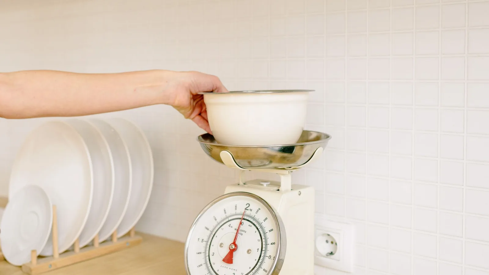 Close-up of hand placing a bowl on a kitchen weighing scale for food preparation.
