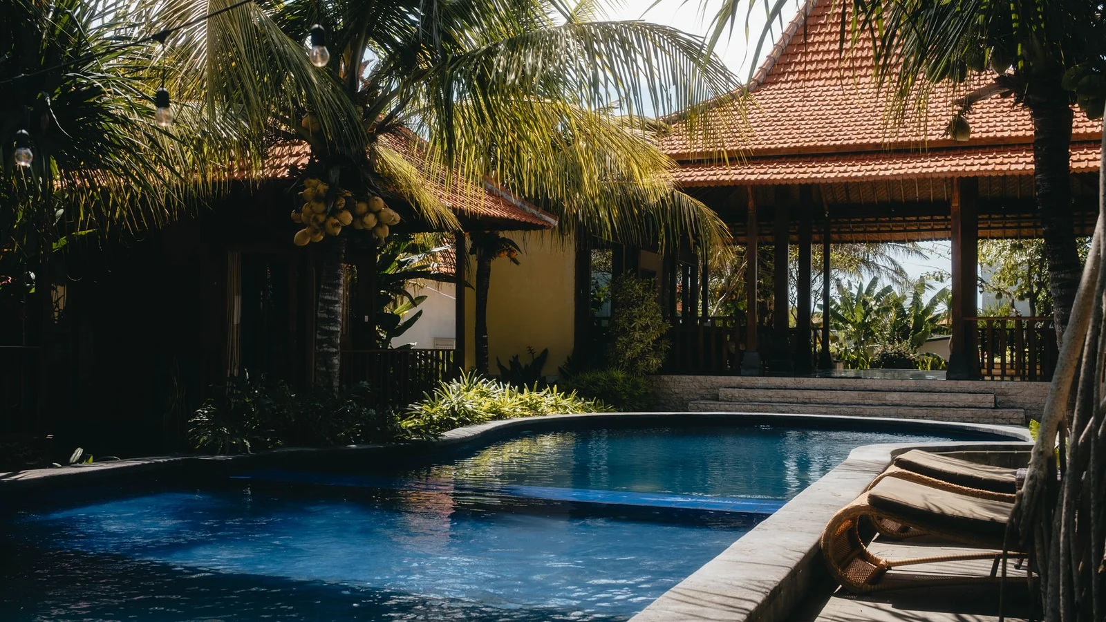 Relax by a luxurious tropical pool surrounded by lush palm trees under a sunny sky, perfect for summer getaways.