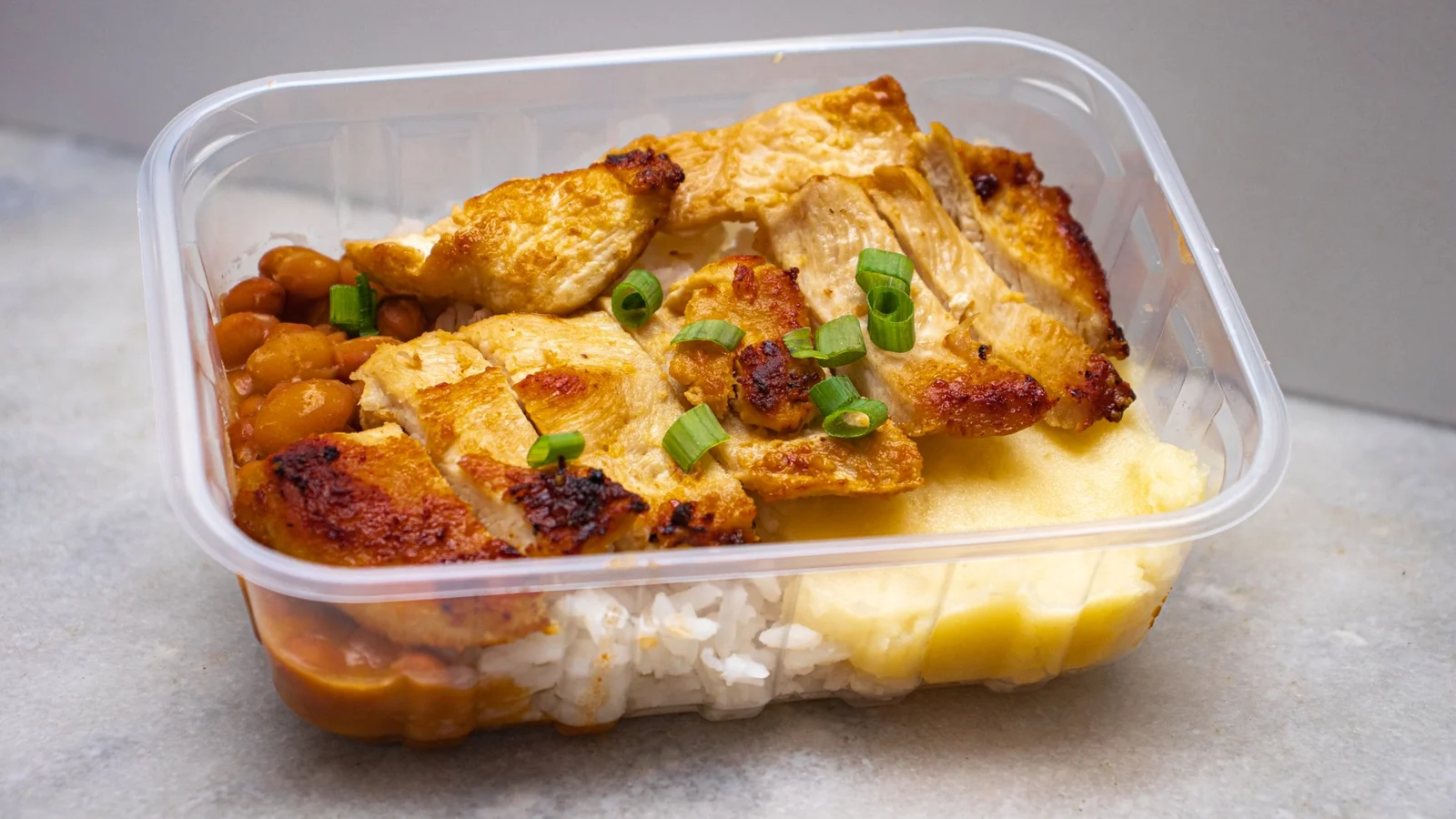 A takeaway container holding cooked rice and a prepared meal.