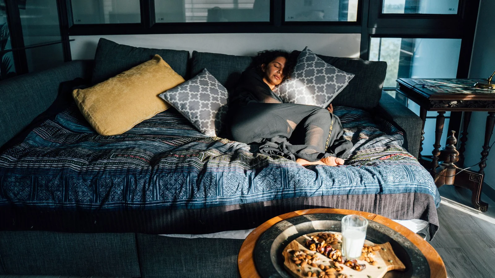 A woman resting on a bed in a sunlit room.