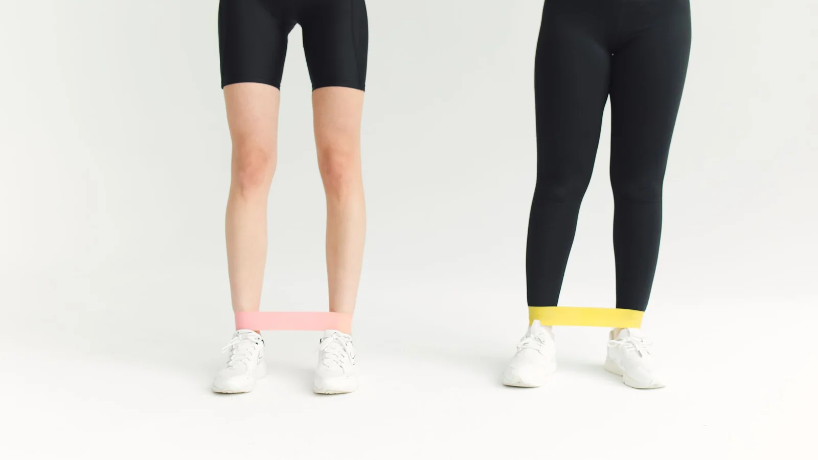 Two women exercising with short resistance bands.