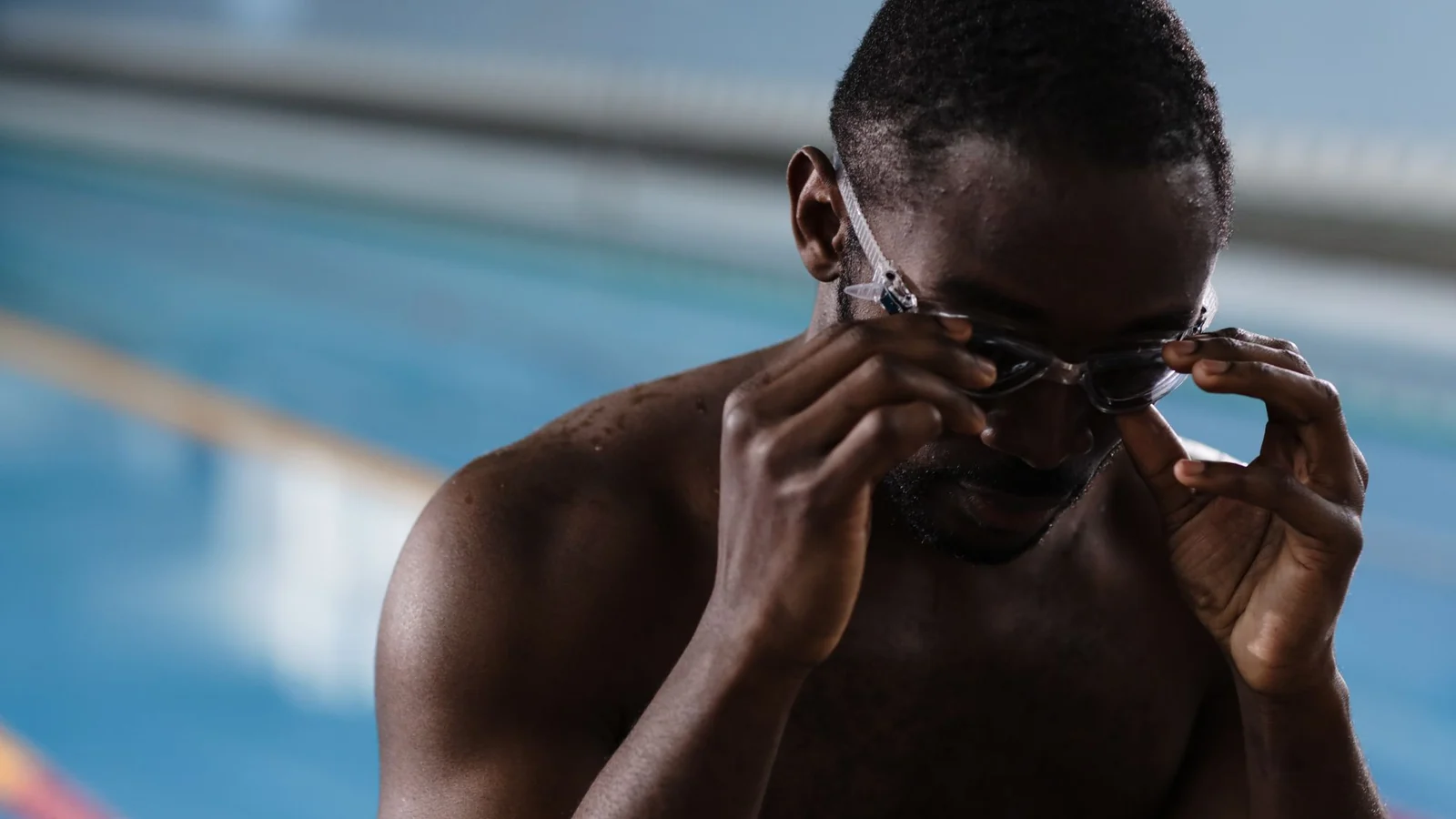 A swimmer adjusting goggles beside a pool; illustrative stock photograph.