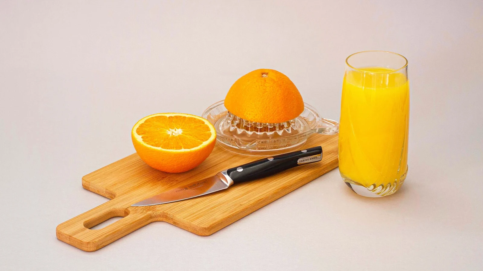 Whole and cut oranges beside a glass of orange juice.