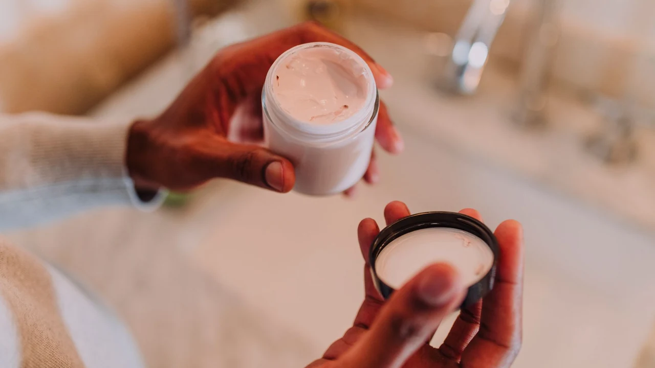 Hands holding an open jar of pink cream