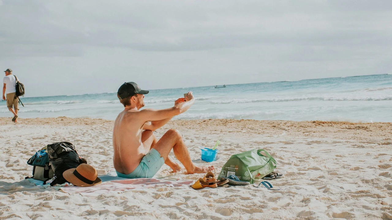 Man seated on a beach beside a bag and towel