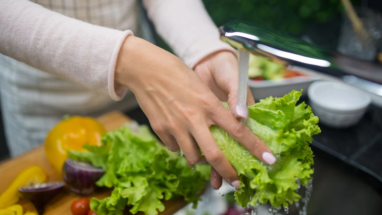 Hands rinsing lettuce under running water.