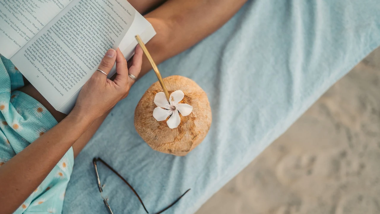 Person reading a book beside a coconut drink.