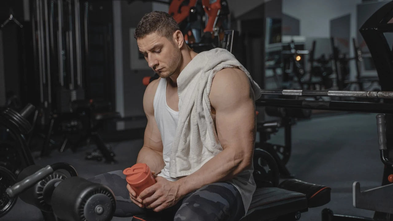 Man seated in a gym holding a shaker bottle.