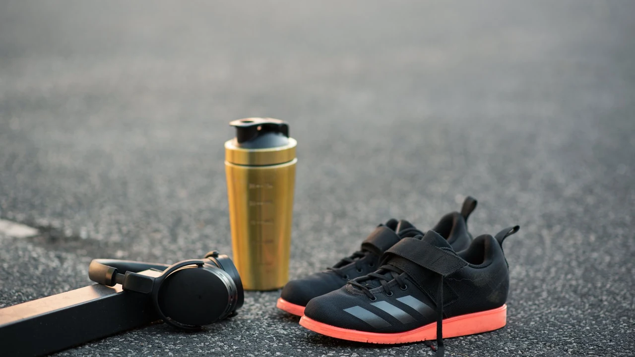 Training shoes, headphones and a yellow bottle on pavement.