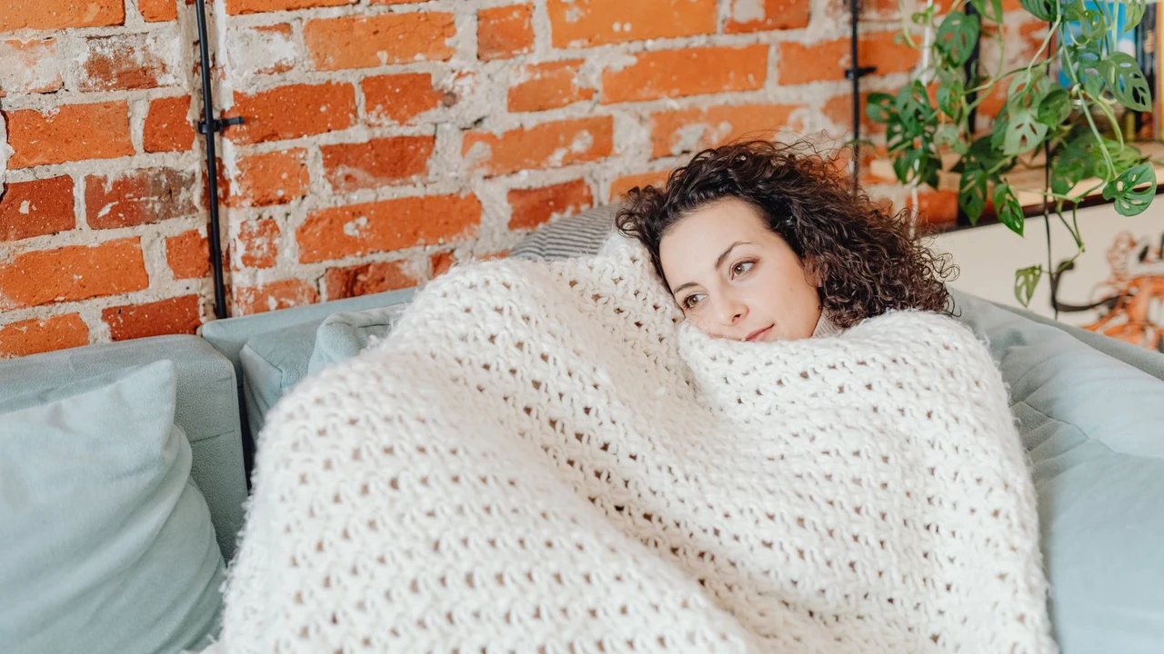 Woman wrapped in a blanket on a sofa.