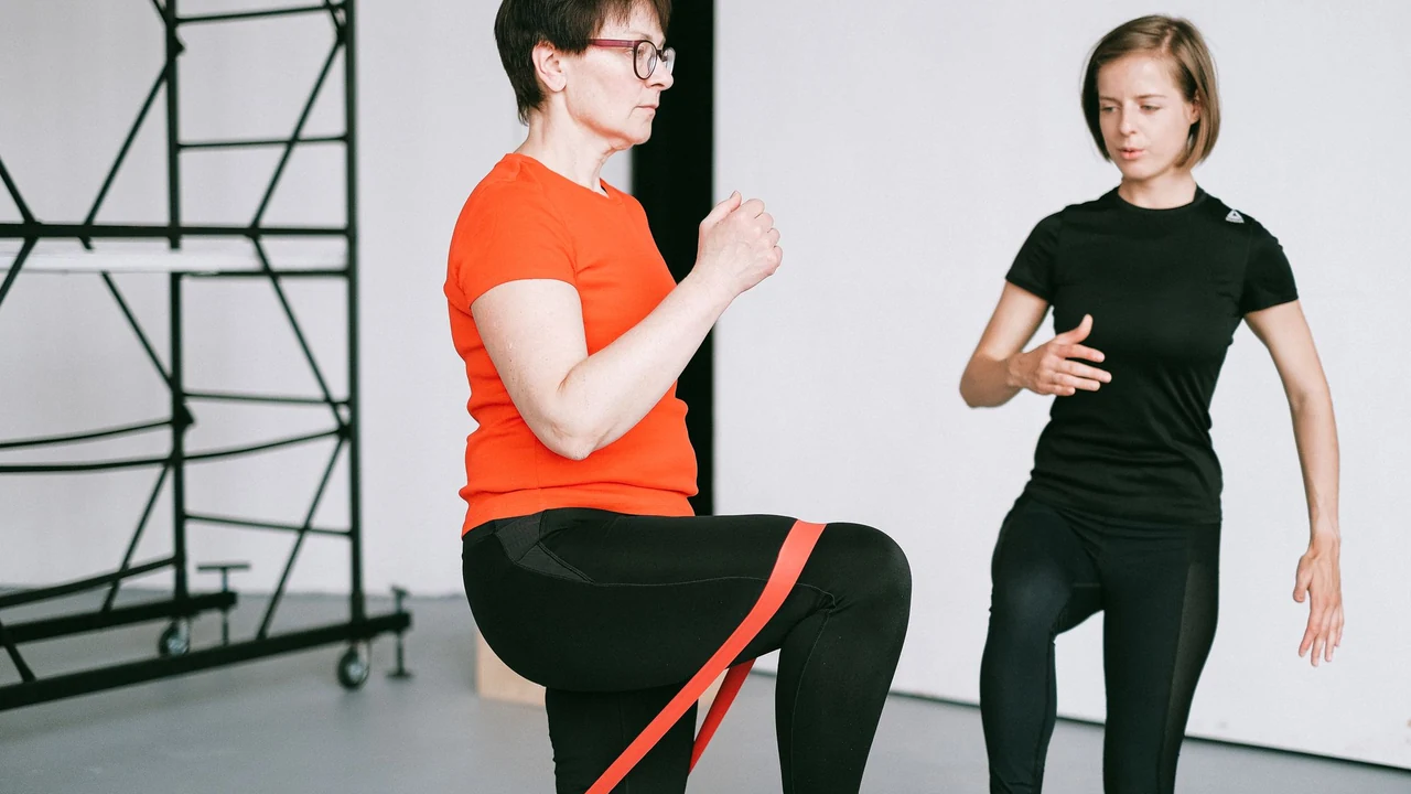 Older woman exercising with a resistance band beside a trainer.