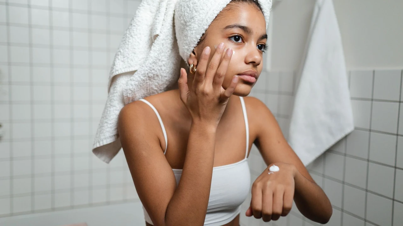 Woman applying face cream while wearing a towel around her hair.