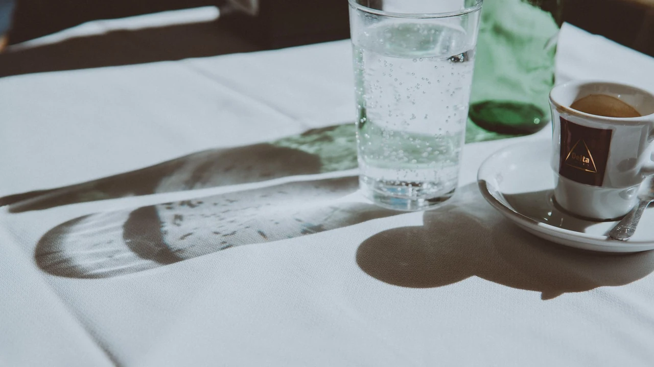 Glass of sparkling water and coffee cup on a restaurant table.