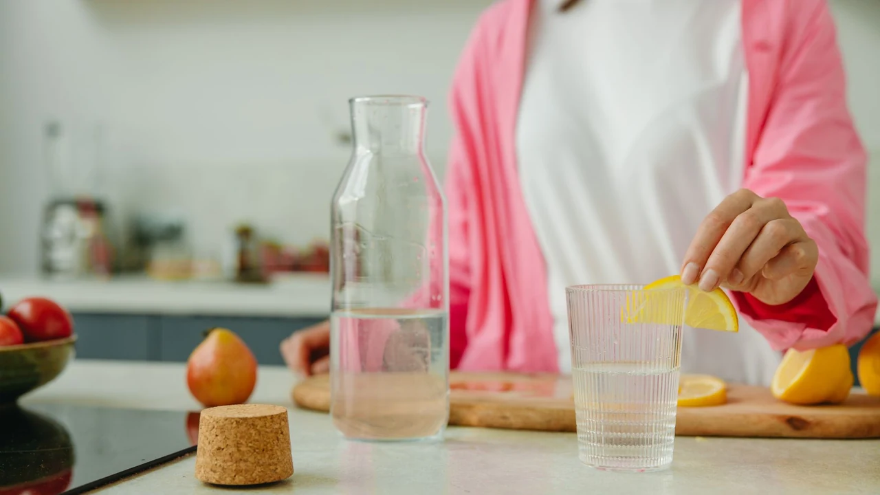 Person adding lemon to a glass of water.