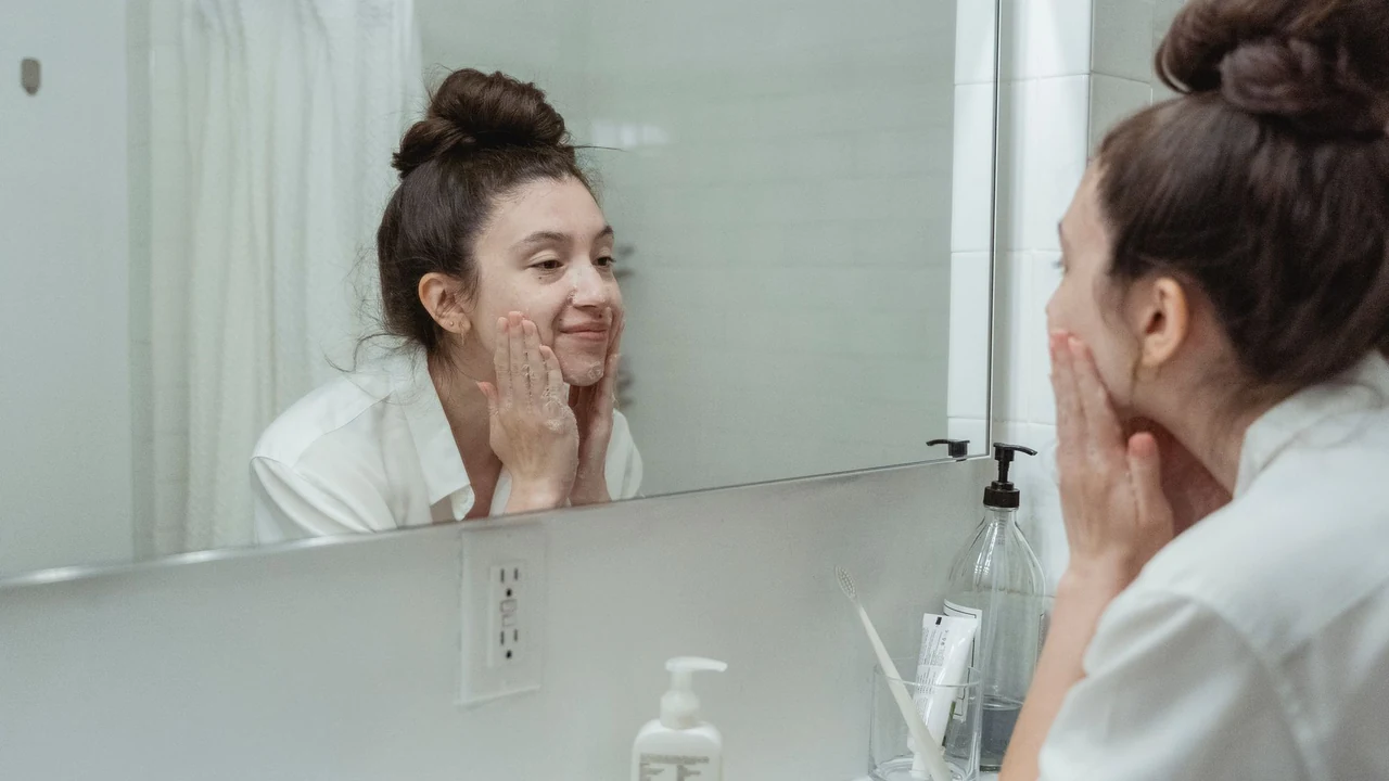 A woman gently cleansing her face in front of a mirror