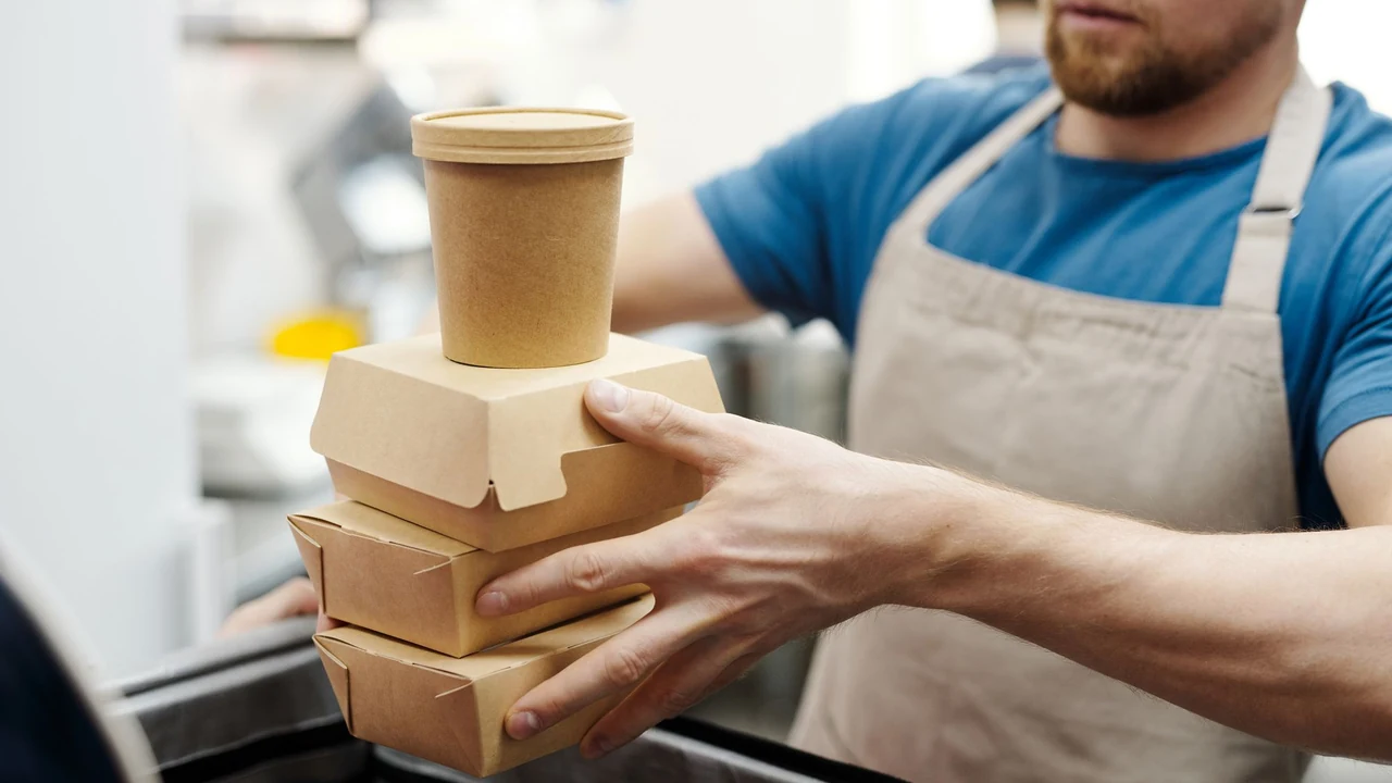 A restaurant worker holding takeaway boxes and a paper cup